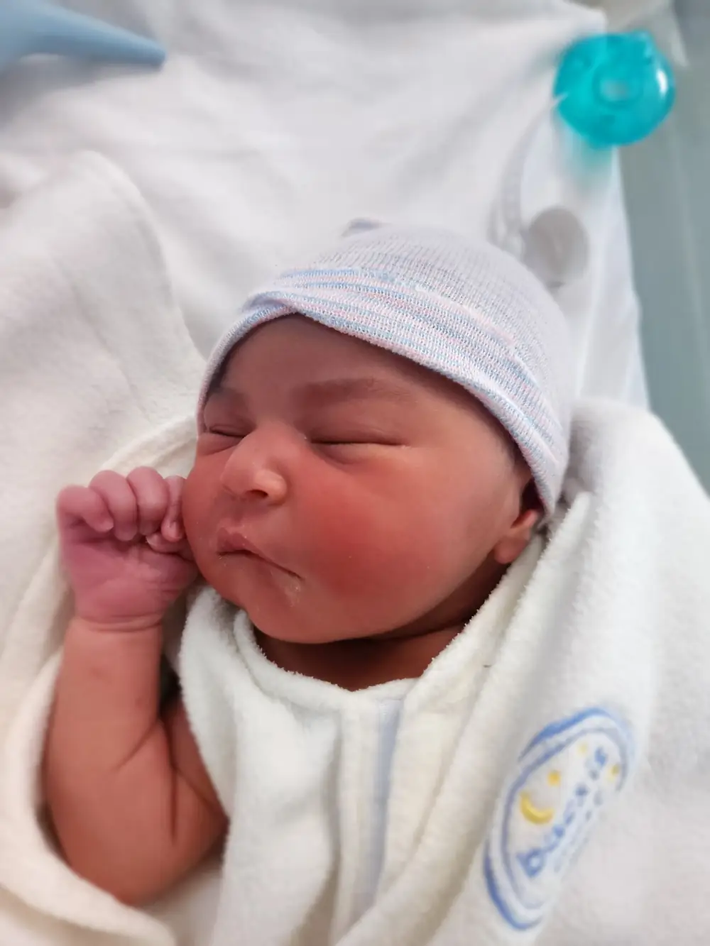 Un recién nacido duerme envuelto en una manta, con su gorrito del hospital